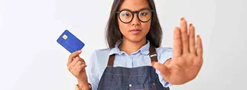 Mulher de macacão e óculos, segurando em uma mão um cartão de crédito e com a outra mão ela faz um sinal de PARE!