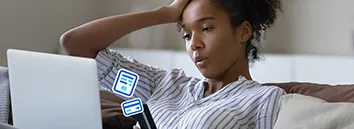 Mulher sentada no sofá. Com a mão na cabeça ela olha confusa para um notebook que está em seu colo.